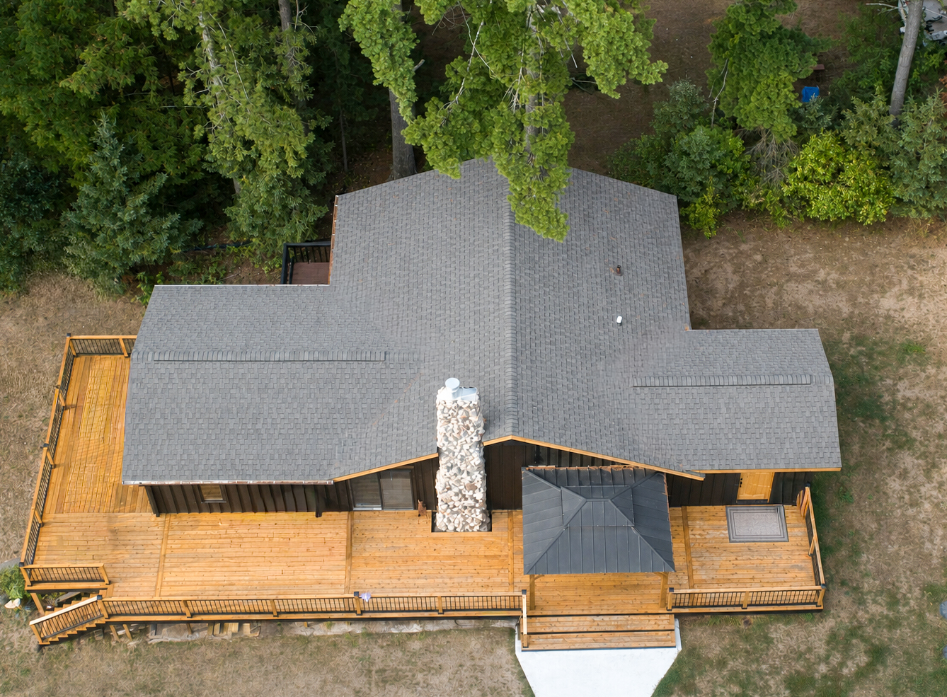 Aerial view of a cabin roof with stone chimney, wraparound deck and new shingles