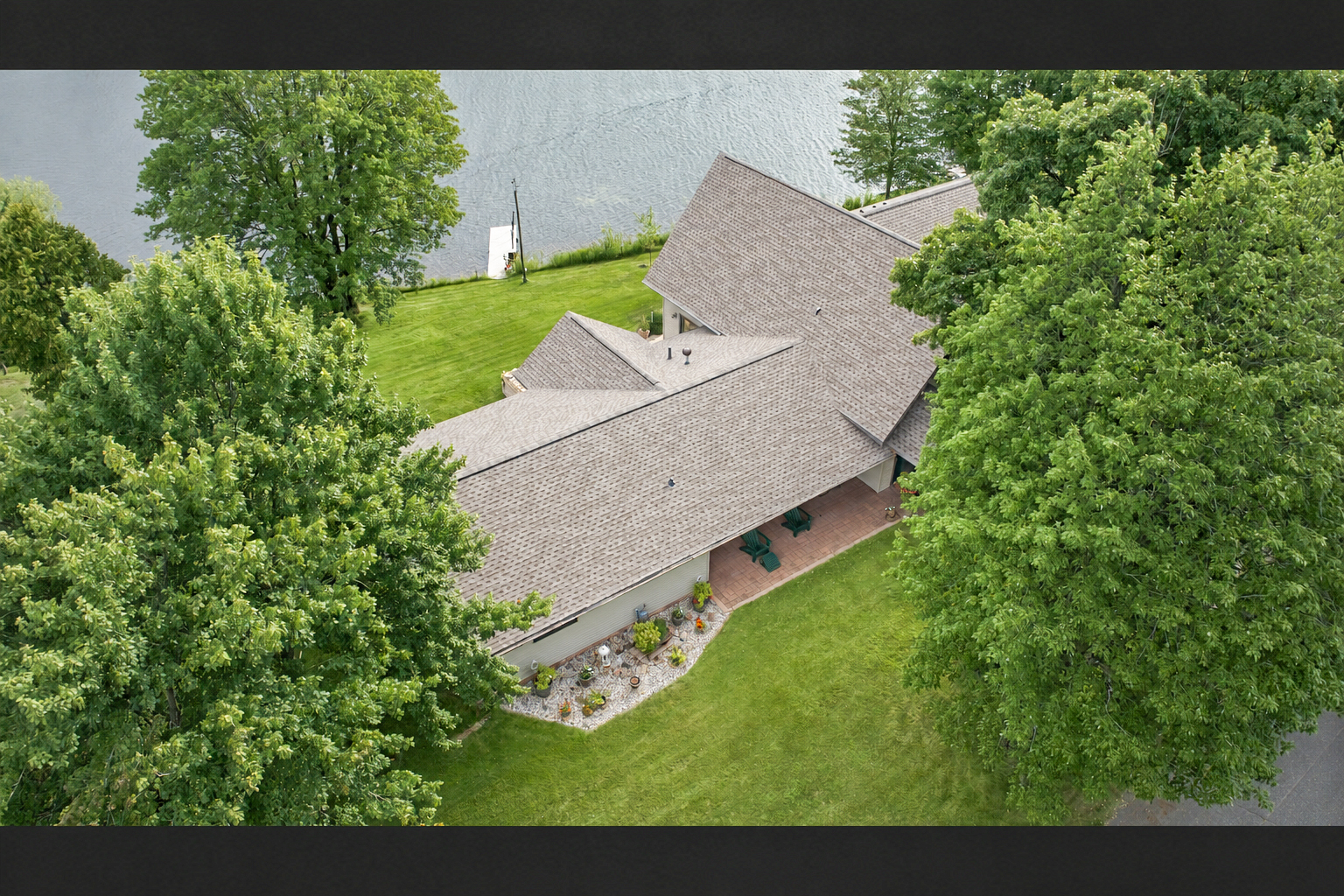 Aerial view through mature trees toward a completed shingle roof near the water